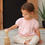 A child sitting on a blue and white rug playing with the Plan Toys Natural Stacking Ring.