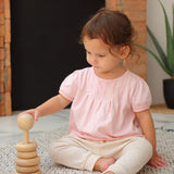 A child sitting on a blue and white rug playing with the Plan Toys Natural Stacking Ring.