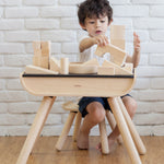 A child sat at a PlanToys desk  playing with the Plan Toys natural wooden 50 Unit Building Block. set.