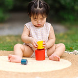 Child playing with the PlanToys Nesting Cylinders 3 piece wooden toy. Red, yellow and blue coloured wooden cylinder shaped wooden pieces that nest inside each other. 