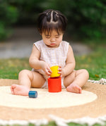 Child playing with the PlanToys Nesting Cylinders 3 piece wooden toy. Red, yellow and blue coloured wooden cylinder shaped wooden pieces that nest inside each other. 