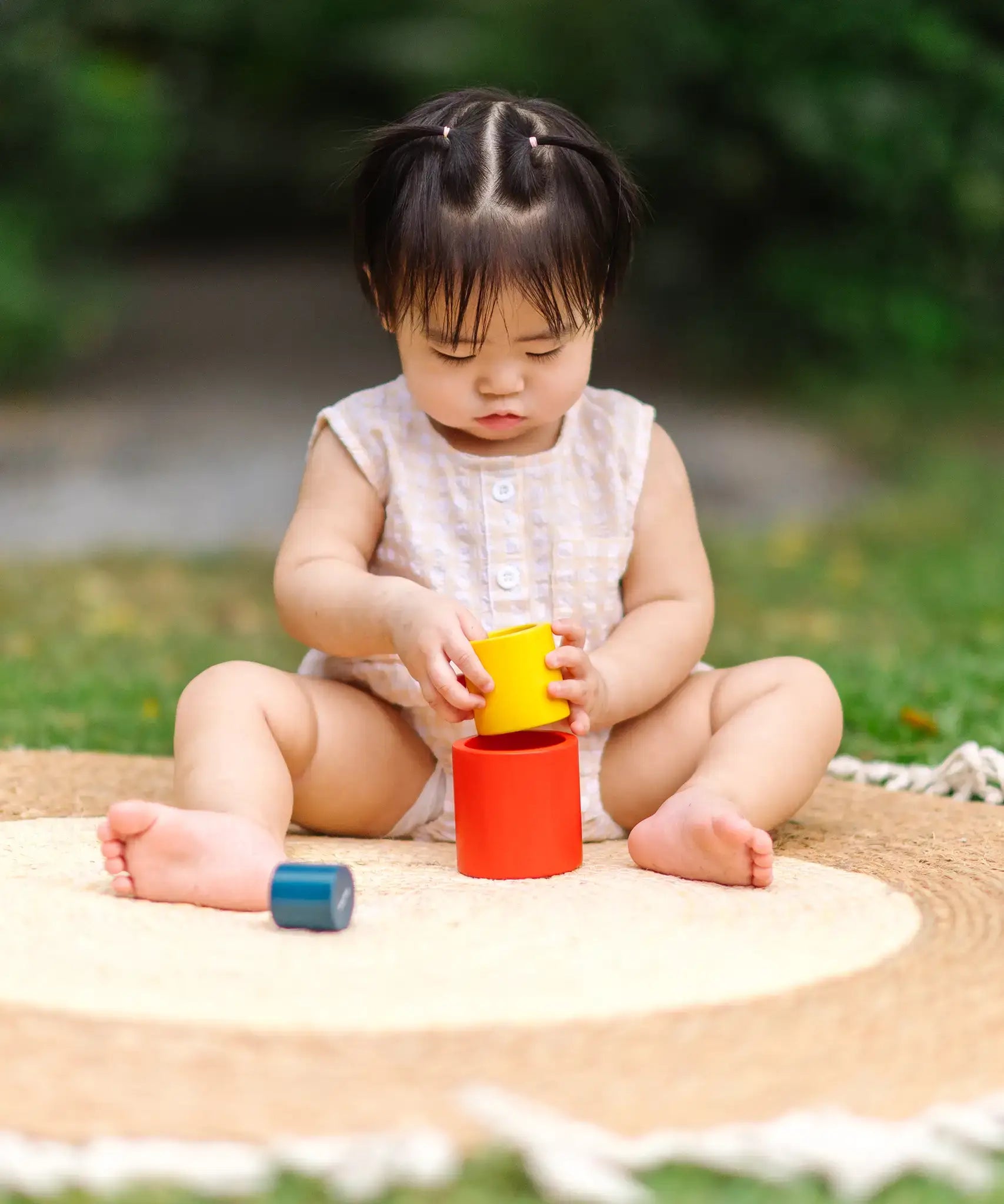 Child playing with the PlanToys Nesting Cylinders 3 piece wooden toy. Red, yellow and blue coloured wooden cylinder shaped wooden pieces that nest inside each other. 