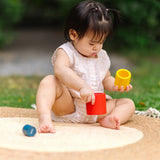 Child playing with the PlanToys Nesting Cylinders 3 piece wooden toy. Red, yellow and blue coloured wooden cylinder shaped wooden pieces that nest inside each other. 