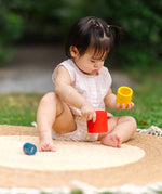 Child playing with the PlanToys Nesting Cylinders 3 piece wooden toy. Red, yellow and blue coloured wooden cylinder shaped wooden pieces that nest inside each other. 