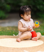 Child playing with the PlanToys Nesting Cylinders 3 piece wooden toy. Red, yellow and blue coloured wooden cylinder shaped wooden pieces that nest inside each other. 