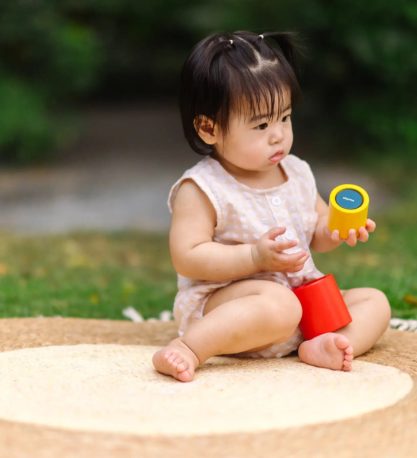 Child playing with the PlanToys Nesting Cylinders 3 piece wooden toy. Red, yellow and blue coloured wooden cylinder shaped wooden pieces that nest inside each other. 