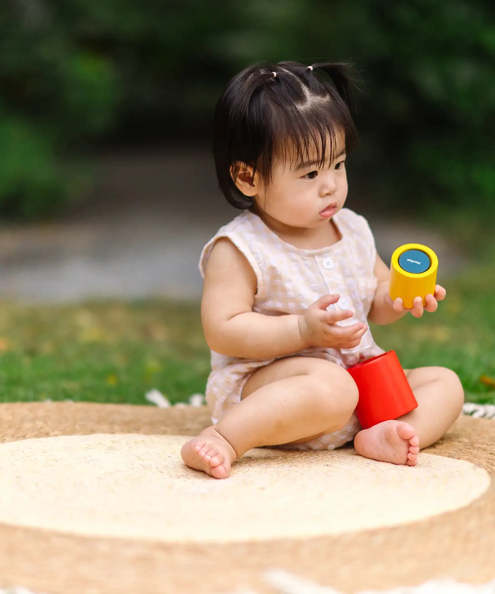 Child playing with the PlanToys Nesting Cylinders 3 piece wooden toy. Red, yellow and blue coloured wooden cylinder shaped wooden pieces that nest inside each other. 