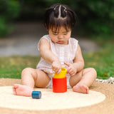 Child playing with the PlanToys Nesting Cylinders 3 piece wooden toy. Red, yellow and blue coloured wooden cylinder shaped wooden pieces that nest inside each other. 
