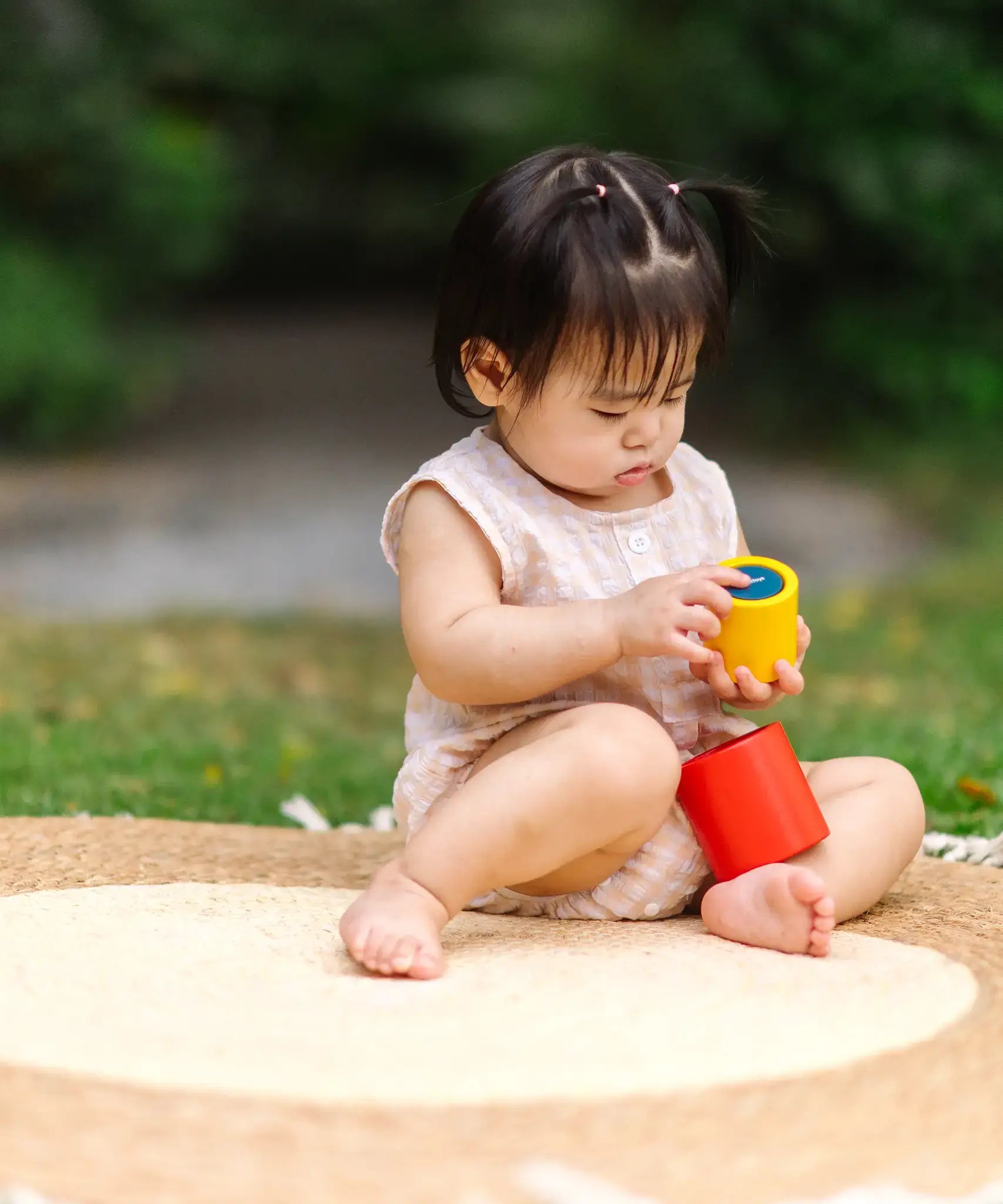 Child playing with the PlanToys Nesting Cylinders 3 piece wooden toy. Red, yellow and blue coloured wooden cylinder shaped wooden pieces that nest inside each other. 