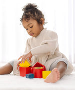 Child playing with PlanToys nesting boxes, triangles and cylinders.