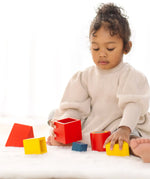 Child playing with PlanToys nesting boxes, triangles and cylinders.