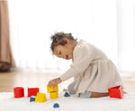 Child playing with PlanToysnesting boxes, triangles and cylinders.
