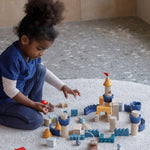 A child playing sitting on a rug playing with the PlanToys Castle Building Blocks set. 