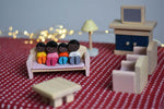 A family of PlanToys peg dolls sitting on the wooden dollhouse sofa amongst other living room furniture. 
