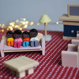 A family of PlanToys peg dolls sitting on the wooden dollhouse sofa amongst other living room furniture. 
