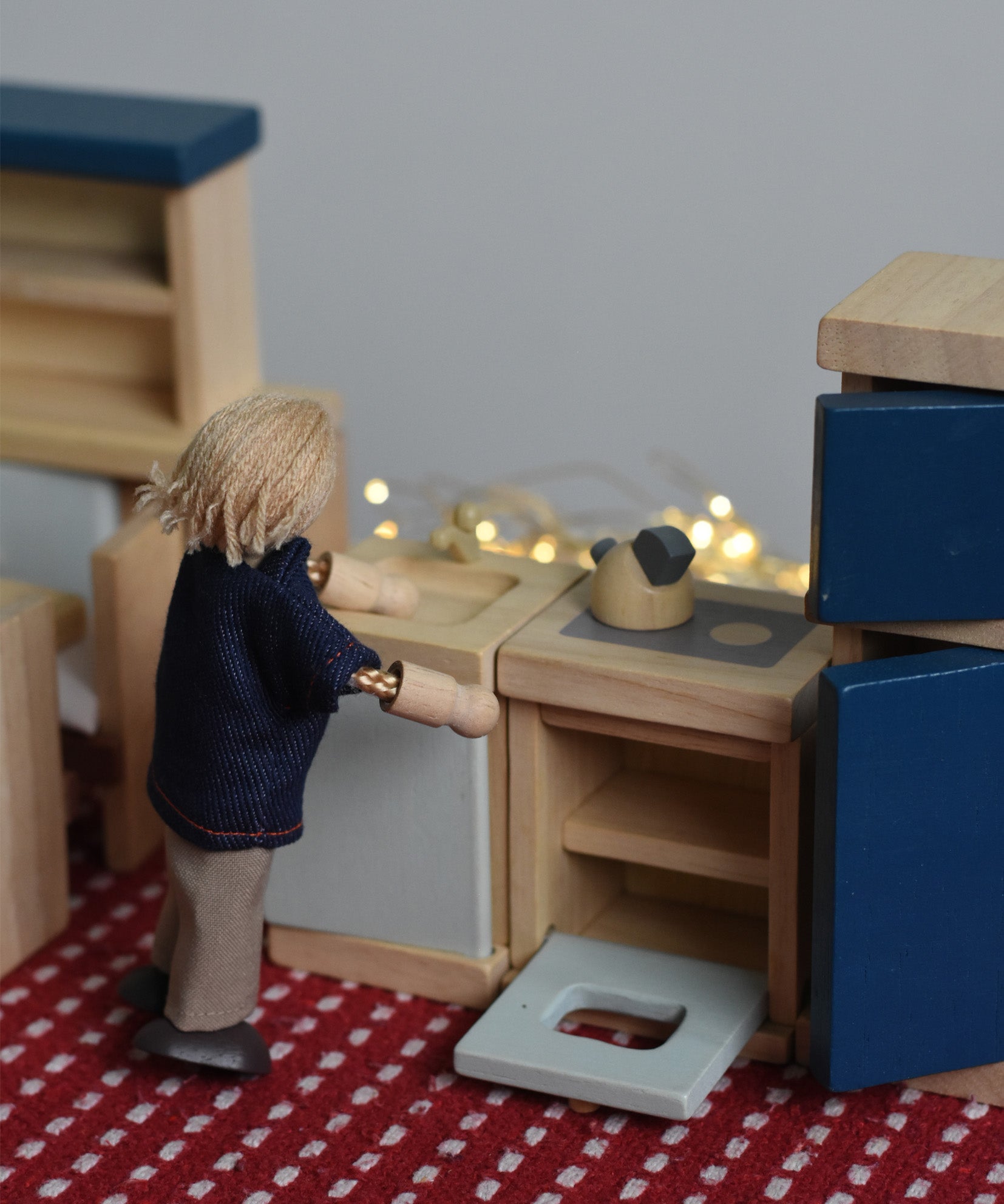 A PlanToys peg doll positioned in a small-world play scene, using the wooden dollhouse kitchen furniture.