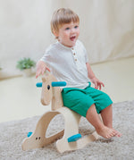 A child sitting on the side of the PlanToys Palomino Rocking Horse. 