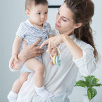 An adult holding a baby in one arm and a PlanToys Pastel Baby Key Rattle in the other hand. 
