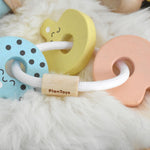 A PlanToys Pastel Baby Key Rattle toy placed on a sheepskin rug. 