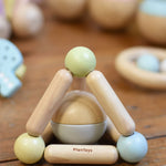 A PlanToys Pastel Triangle Clutching Toy placed on a wooden floor surrounded by other toys from the PlanToys pastel baby collection. 