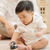 A baby sitting and reaching for the PlanToys Penguin Wobbler wooden baby toy. A circular shaped penguin toy that wobbles when placed on a flat surface. PlanToys range of toys are made from sustainably sourced rubberwood, we're proud stockists of PlanToys here at Babipur. 