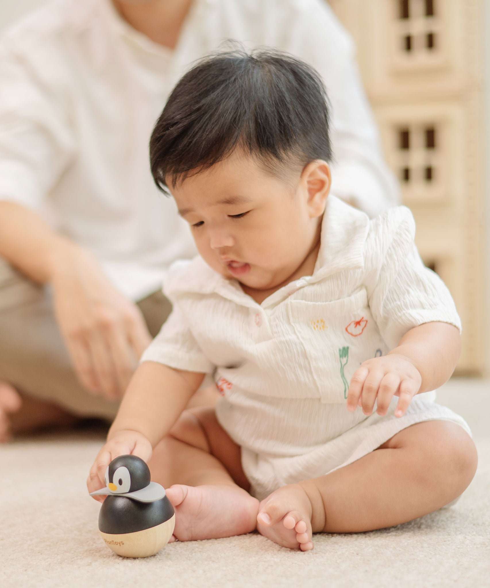 A baby sitting and reaching for the PlanToys Penguin Wobbler wooden baby toy. A circular shaped penguin toy that wobbles when placed on a flat surface. PlanToys range of toys are made from sustainably sourced rubberwood, we're proud stockists of PlanToys here at Babipur. 