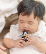 A baby holding the PlanToys Penguin Wobbler wooden baby toy. A circular shaped penguin toy that wobbles when placed on a flat surface. PlanToys range of toys are made from sustainably sourced rubberwood, we're proud stockists of PlanToys here at Babipur. 