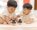 Babies playing with PlanToys Penguin Wobbler wooden baby toy. A circular shaped penguin toy that wobbles when placed on a flat surface. PlanToys range of toys are made from sustainably sourced rubberwood, we're proud stockists of PlanToys here at Babipur. 