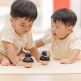 Babies playing with PlanToys Penguin Wobbler wooden baby toy. A circular shaped penguin toy that wobbles when placed on a flat surface. PlanToys range of toys are made from sustainably sourced rubberwood, we're proud stockists of PlanToys here at Babipur. 