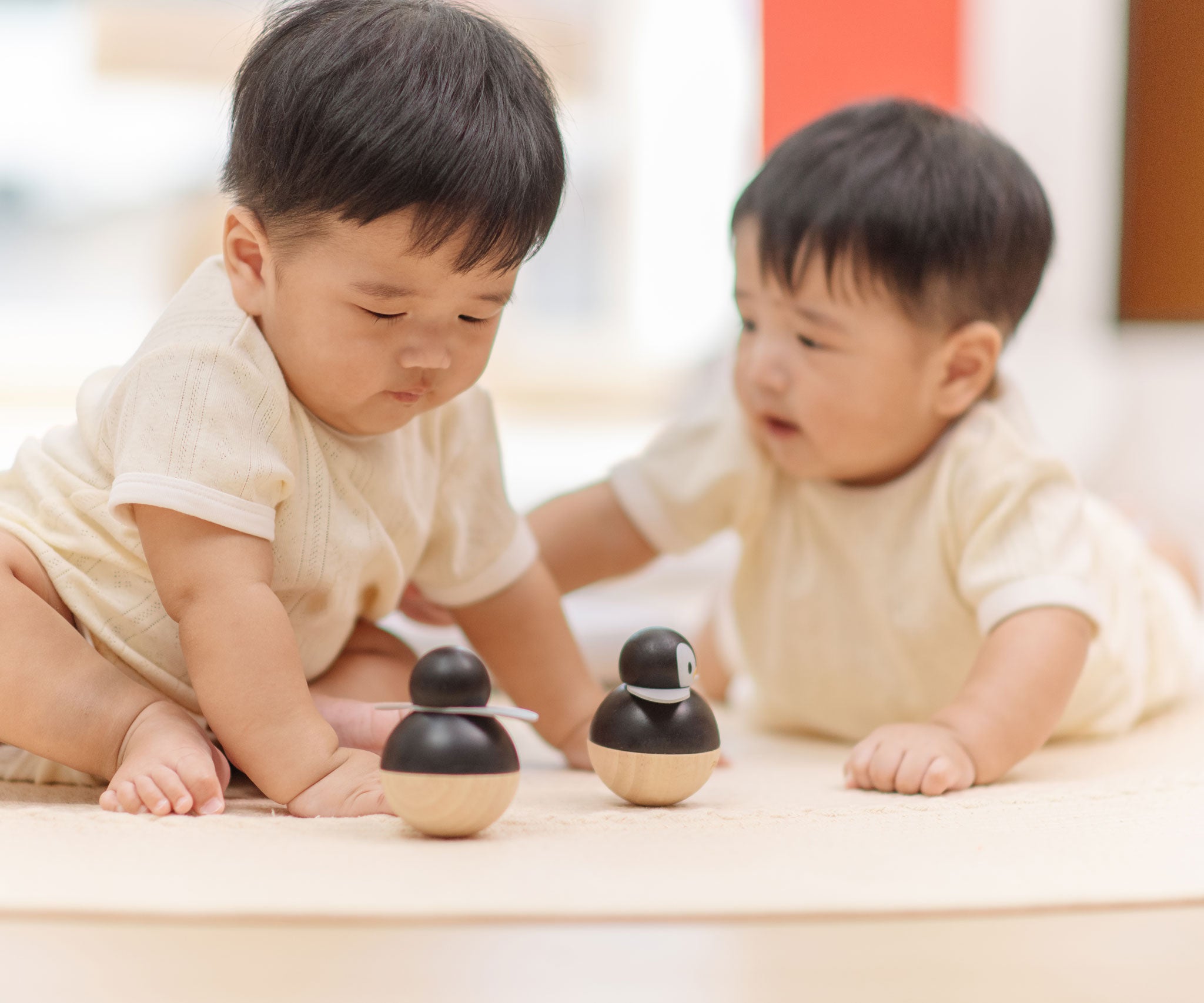 Babies playing with PlanToys Penguin Wobbler wooden baby toy. A circular shaped penguin toy that wobbles when placed on a flat surface. PlanToys range of toys are made from sustainably sourced rubberwood, we're proud stockists of PlanToys here at Babipur. 