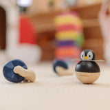A PlanToys Penguin Wobbler wooden baby toy placed next to other wooden toys. A circular shaped penguin toy that wobbles when placed on a flat surface. PlanToys range of toys are made from sustainably sourced rubberwood, we're proud stockists of PlanToys here at Babipur. 