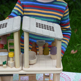 A close up of the PlanToys PlanSpace bathroom placed on top of the kitchen diner set next to the bedroom set. A child can be seen in the background placing peg dolls around the different areas in the house.