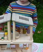 A close up of the PlanToys PlanSpace bathroom placed on top of the kitchen diner set next to the bedroom set. A child can be seen in the background placing peg dolls around the different areas in the house.