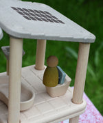 A close up of the green coloured Nin peg doll placed on the toilet from the PlanToys PlanSpace bathroom set.