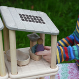 A close up of a child's hand placing a purple Nin peg doll on the toilet from the PlanToys PlanSpace bathroom set.
