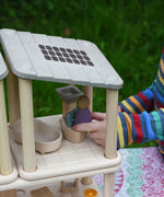 A close up of a child's hand placing a purple Nin peg doll on the toilet from the PlanToys PlanSpace bathroom set.