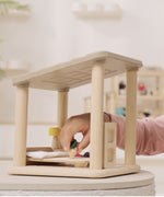 A close up of a child's hand playing with the PlanToys Planspace Bedroom - a wooden open dollhouse.