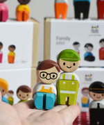 Two dolls from the PlanToys PlanWorld wooden doll service crew in an adult's hand.