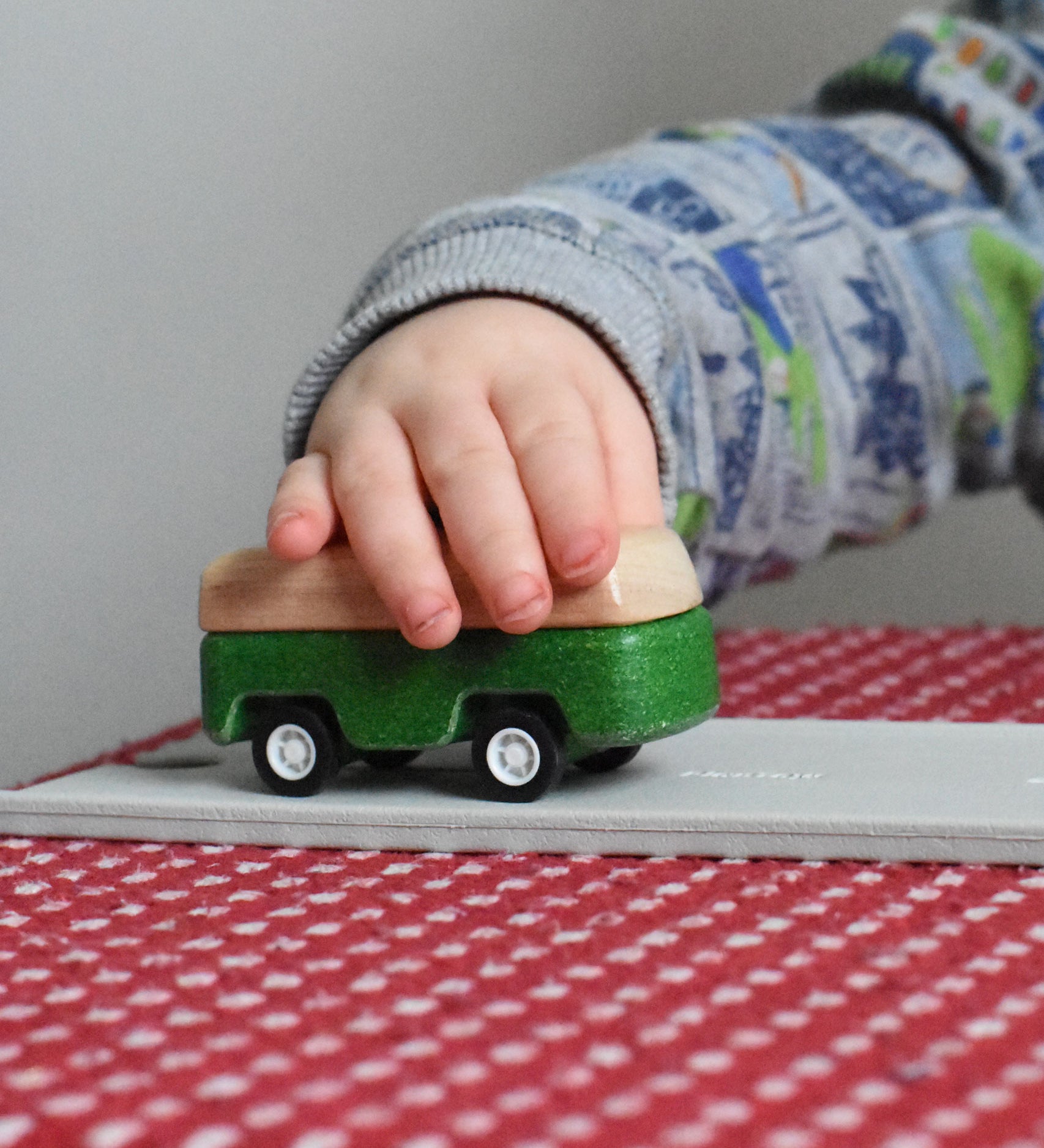 A close up of the green camper from the PlanToys Planworld Cars set being pushed along by a child's hand. 