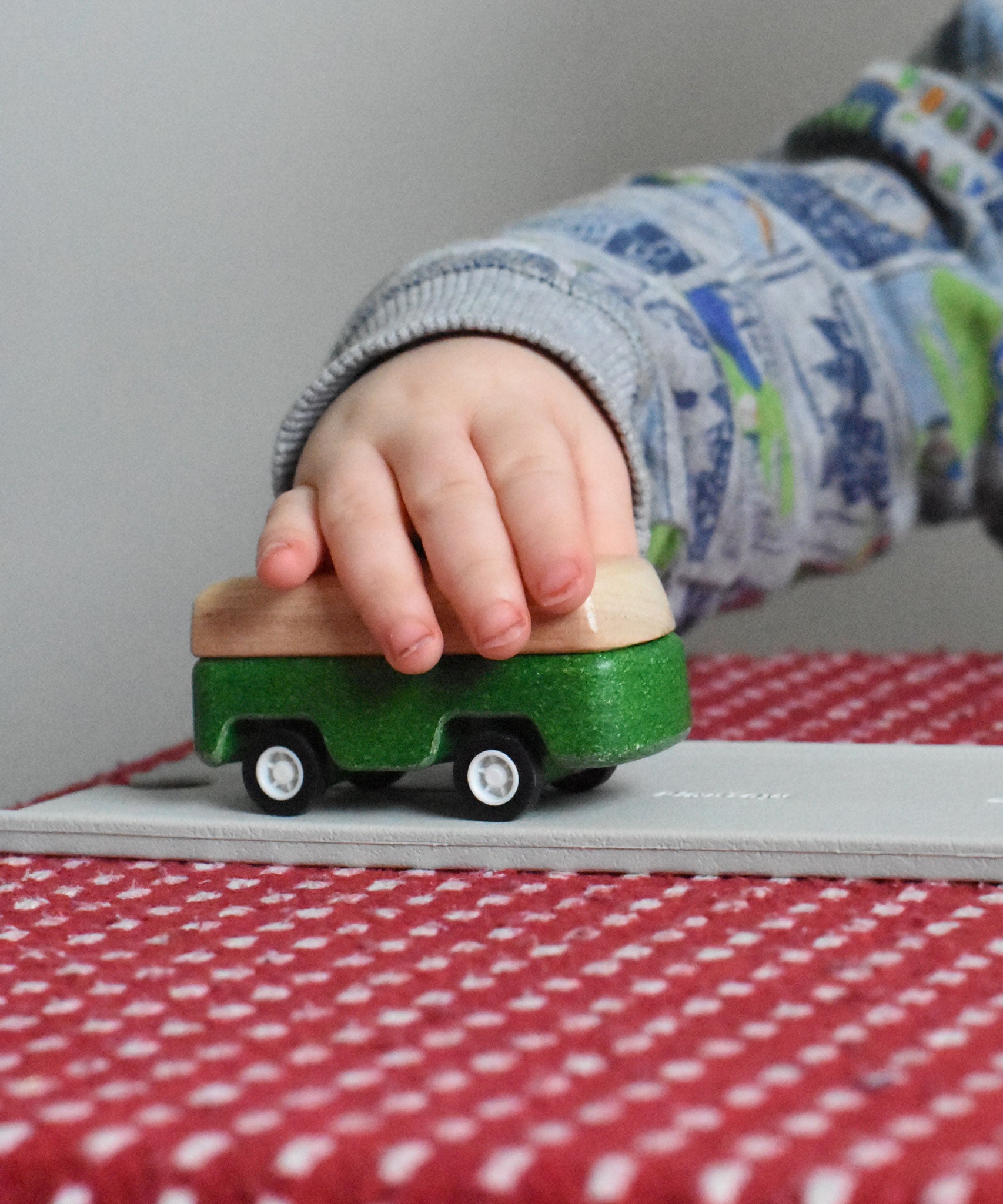 A close up of the green camper from the PlanToys Planworld Cars set being pushed along by a child's hand. 
