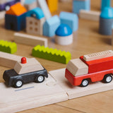 Black police car and red fire engine  from the PlanToys PlanWorld vehicle wooden toy vehicles set placed on a wooden PlanToys road with blocks in the background.