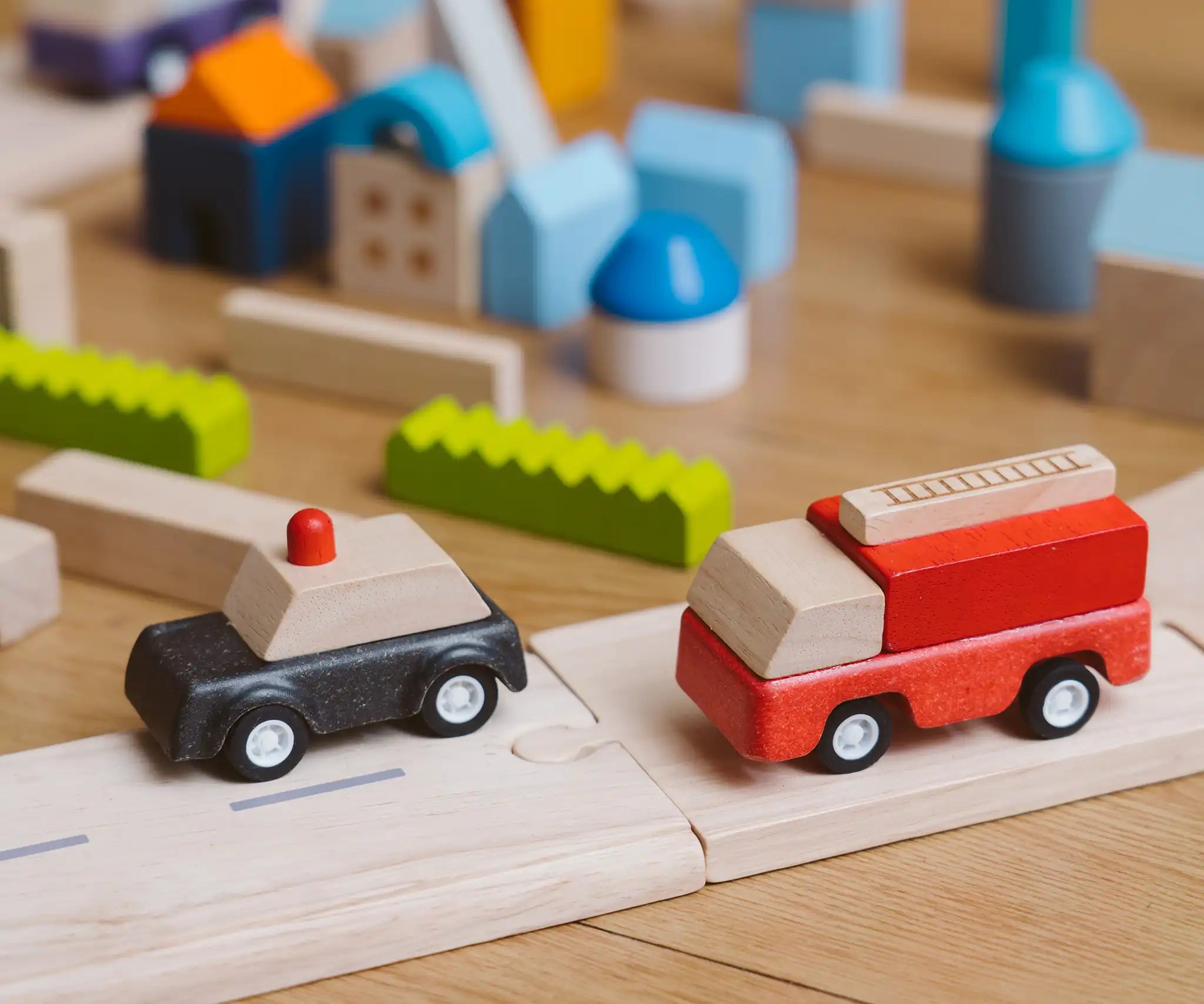 Black police car and red fire engine  from the PlanToys PlanWorld vehicle wooden toy vehicles set placed on a wooden PlanToys road with blocks in the background.