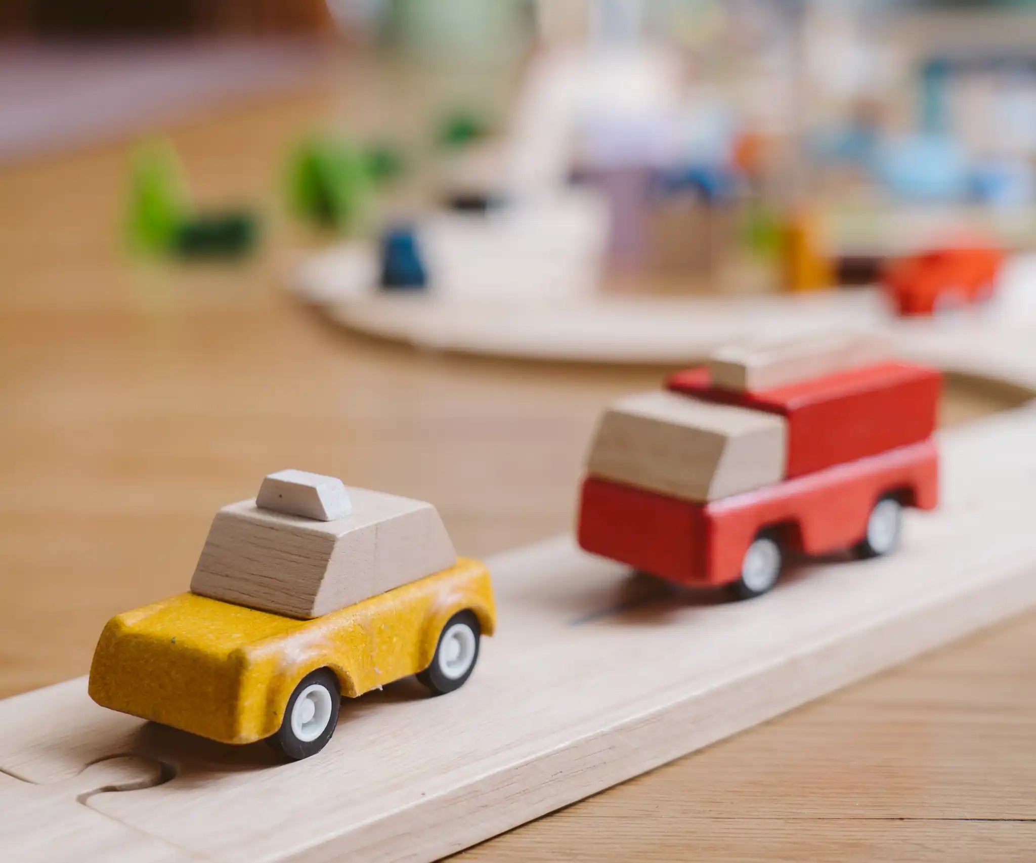 Yellow taxi and red fire engine from the  PlanToys PlanWorld vehicle wooden toy vehicles set placed on a wooden PlanToys road.