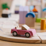 Pink convertible car from the PlanToys PlanWorld vehicle wooden toy vehicles set placed on a wooden PlanToys road.