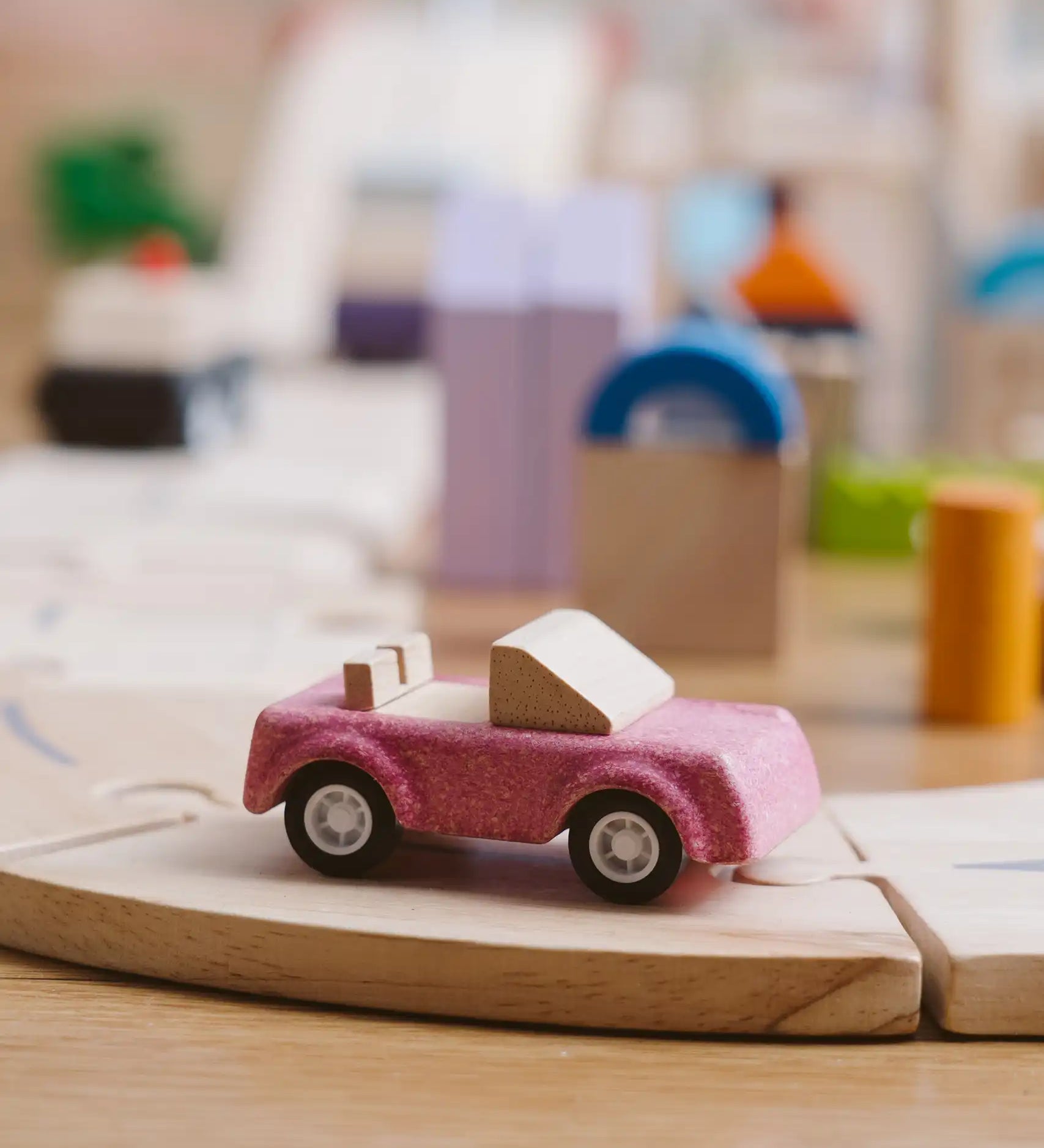 Pink convertible car from the PlanToys PlanWorld vehicle wooden toy vehicles set placed on a wooden PlanToys road.