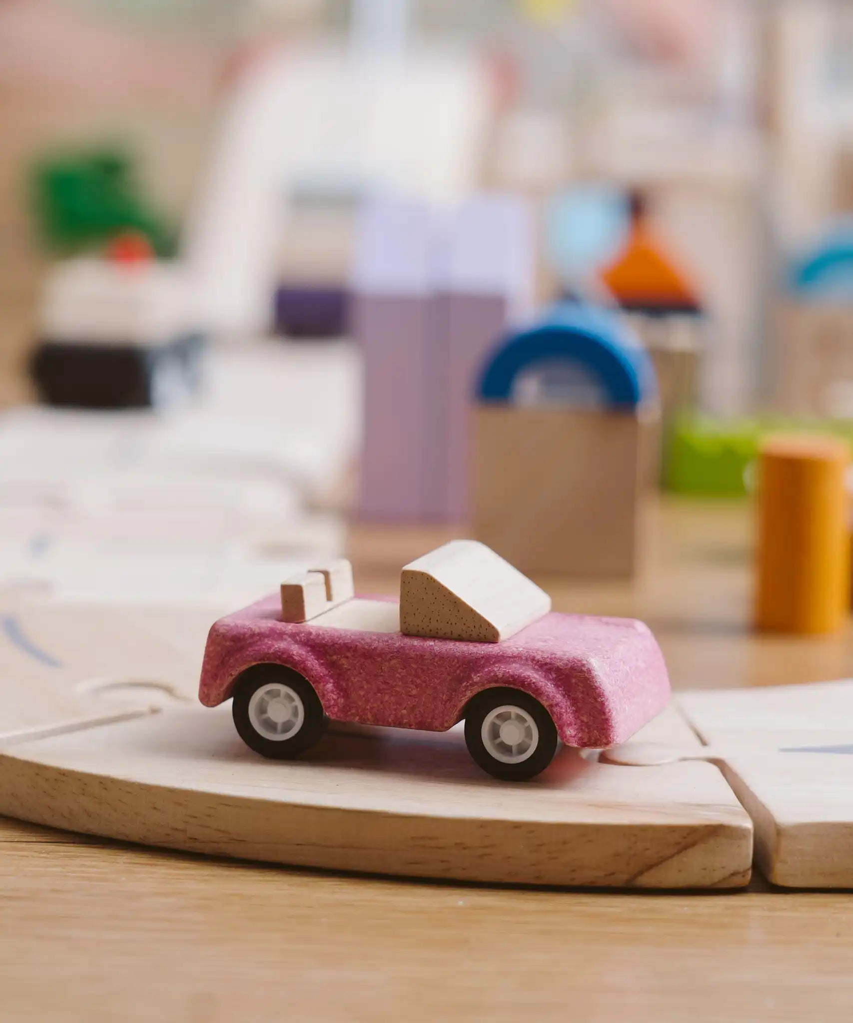 Pink convertible car from the PlanToys PlanWorld vehicle wooden toy vehicles set placed on a wooden PlanToys road.