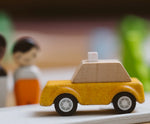 Yellow taxi car from the PlanToys PlanWorld vehicle wooden toy vehicles set placed on a rubber PlanToys road.