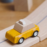 Yellow taxi car from the PlanToys PlanWorld vehicle wooden toy vehicles set placed on a wooden PlanToys road.