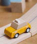 Yellow taxi car from the PlanToys PlanWorld vehicle wooden toy vehicles set placed on a wooden PlanToys road.