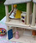 The PlanToys Planspace bedroom shown with two wooden peg dolls, a Grapat Nin and a Grimm's friend laying in the wooden bed covered with a piece of yellow material.